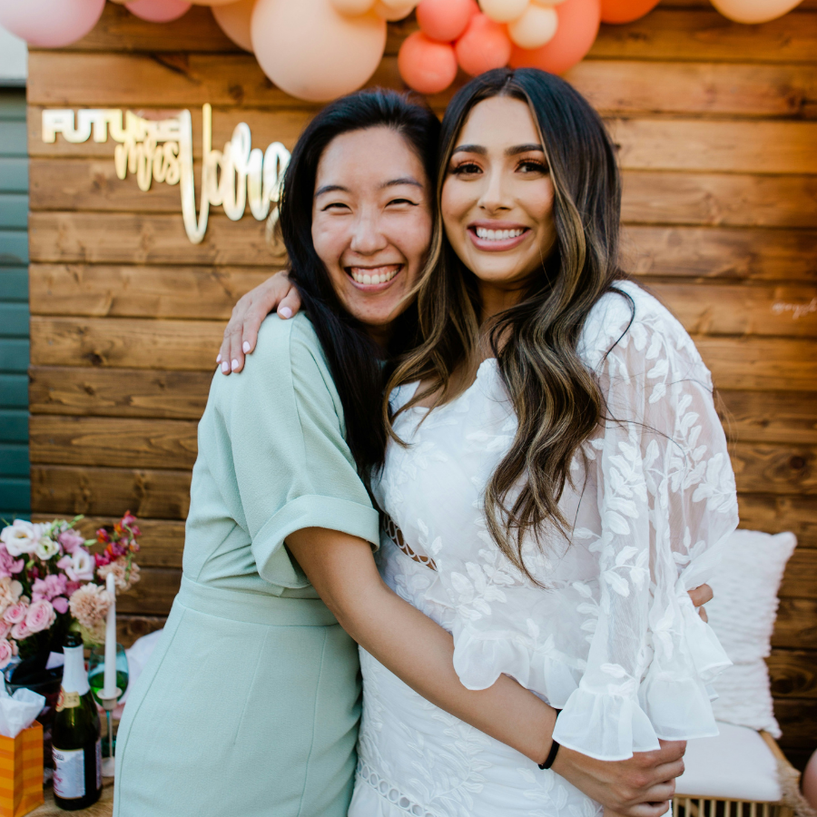 Bride dressed in a white dress hugging a friend and smiling at her bridal shower celebration