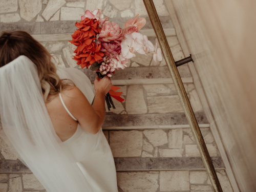 Bride walking up stairs with a pink and red bouquet